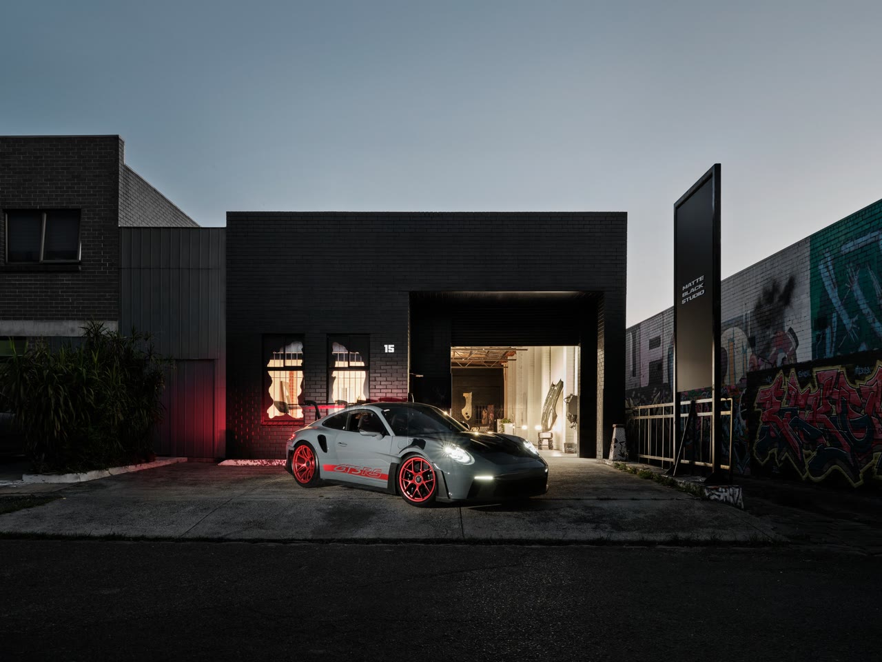 The Matte Black Studio building at dusk, a grey Porsche 911 GT3 RS out front and the roller door open