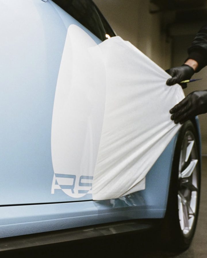 Gloved hands peeling the application tape off white lettering on the door of a Gulf Blue Porsche 911 GT3 Touring