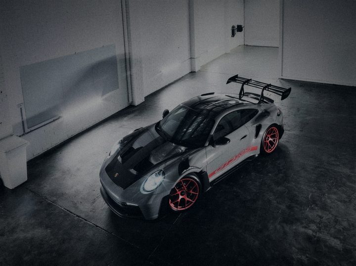 Grey Porsche 911 GT3 RS with a red side script and red wheels, seen from above in a white studio
