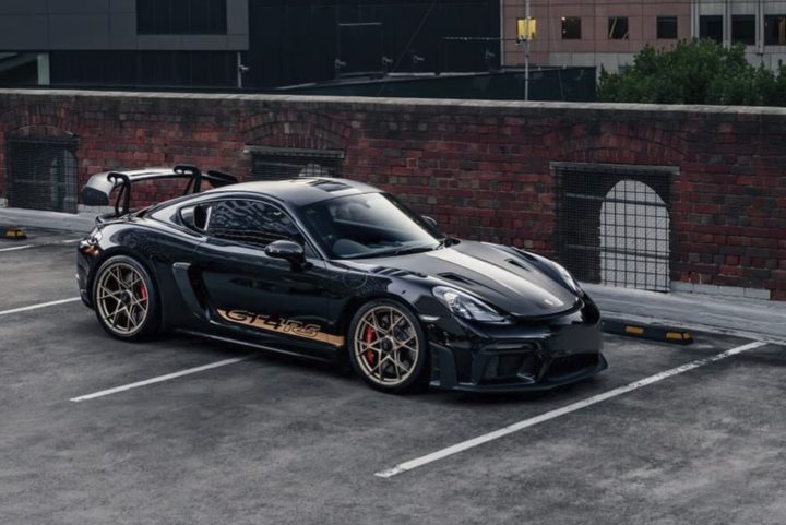 Black Porsche 718 Cayman GT4 RS with gold side stripes on a rooftop car park