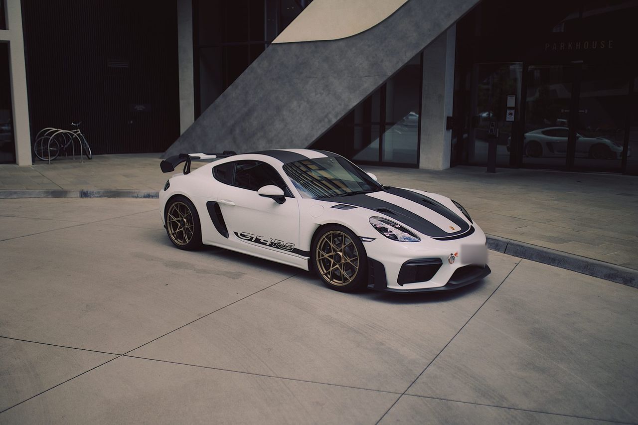 White Porsche 718 Cayman GT4 RS with dark grey bonnet and roof stripes, GT4RS side script and gold wheels