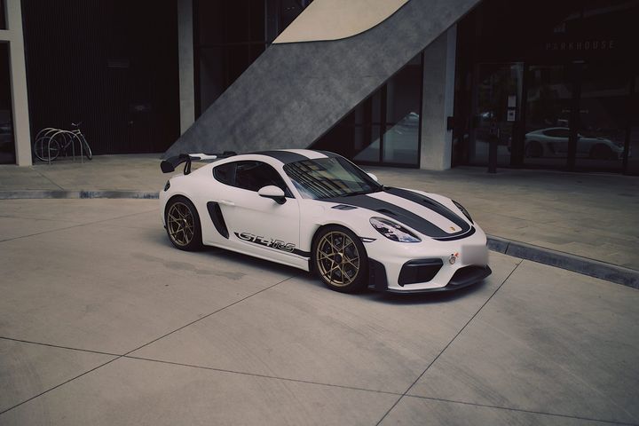 White Porsche 718 Cayman GT4 RS with dark grey bonnet and roof stripes, GT4RS side script and gold wheels