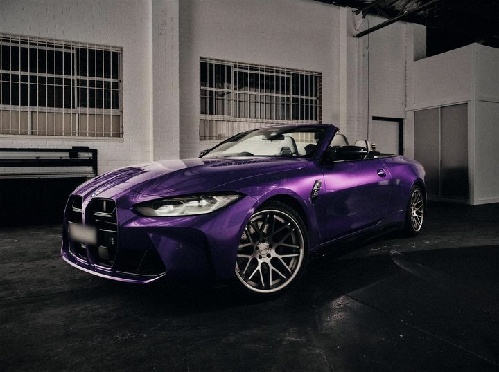Purple BMW M4 Convertible with the roof down in a white brick studio