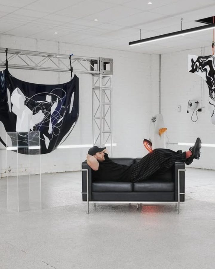 Matt lying on a leather sofa in a white room, among his artworks made from car bonnets and panels