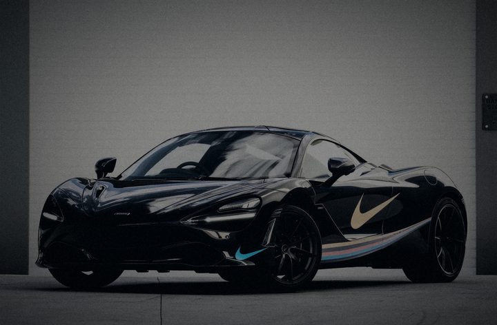 Black McLaren 720S with gold and blue swooshes and a pastel side stripe, in front of a roller door