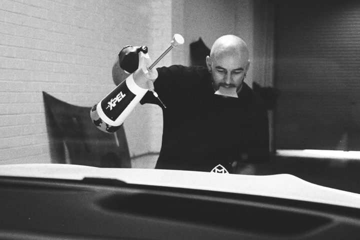 Black and white photo of the installer spraying XPEL solution over a Maybach bonnet before fitting film