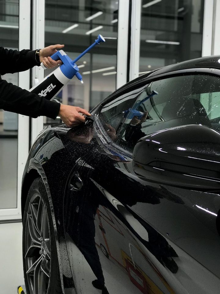 Installer spraying XPEL solution along the window line of a black car before fitting paint protection film