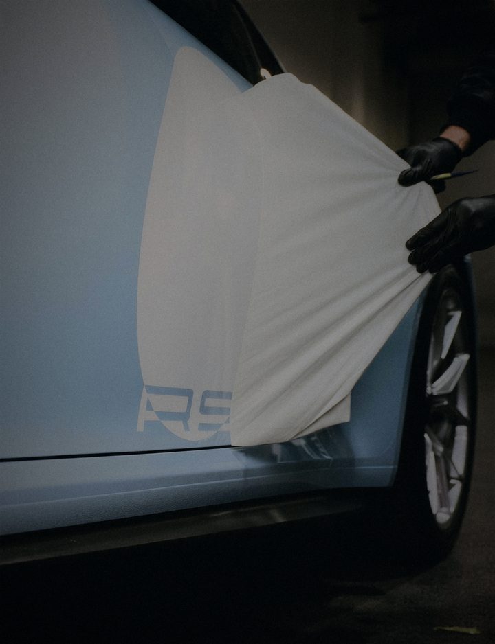 Gloved hands peeling the application tape off white RS lettering on a pale blue car door