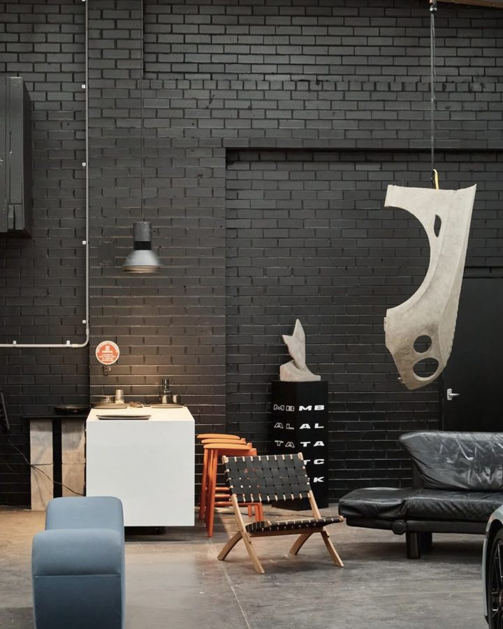 Black brick walls, a sculpted car panel hanging above a leather sofa and chairs